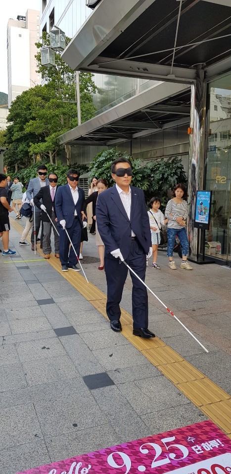 안대를 쓰고 지팡이를 사용하여 걷는 시각장애체험을 하고 있는 참가자들의 모습